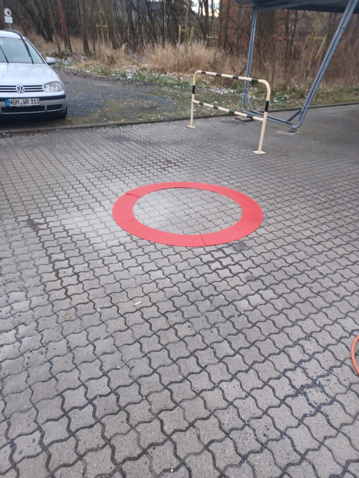 Roter Kreis markiert, auf Pflastersteinen, geparktes Auto und Barriere im Hintergrund. bodenmarkierung-profishop.de